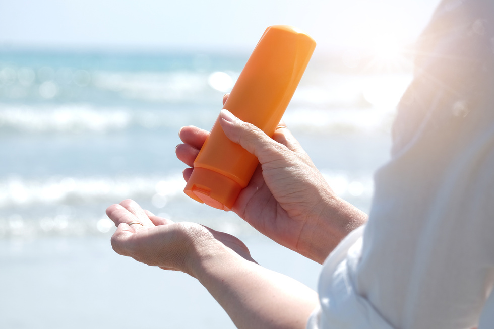Hand of female holding sunscreen. Very sun light Sky background.Health concepts and skin care